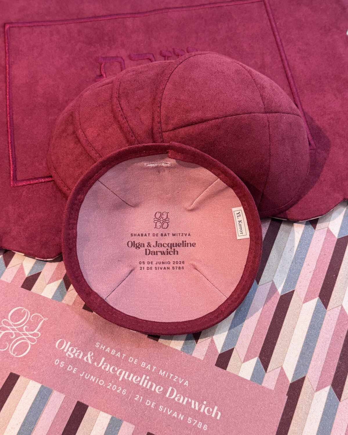 Bat mitzvah kippot color vino sobre mantelería blush con la tarjeta del evento